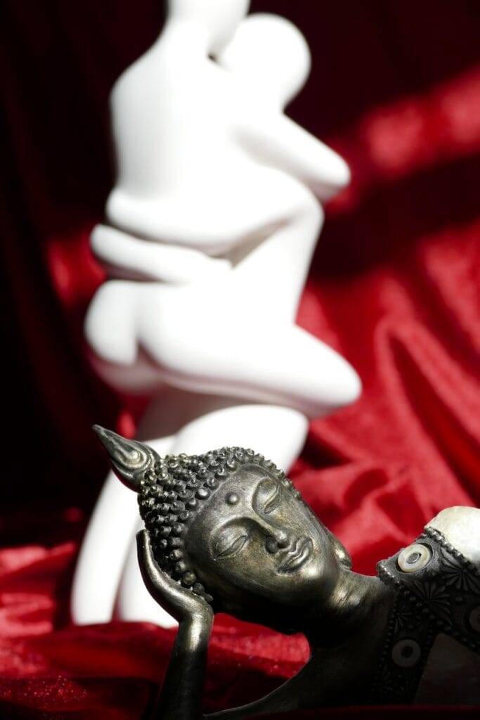 Liegende Buddhastatue auf rotem Samt vor weißer erotischer Paarskulptur