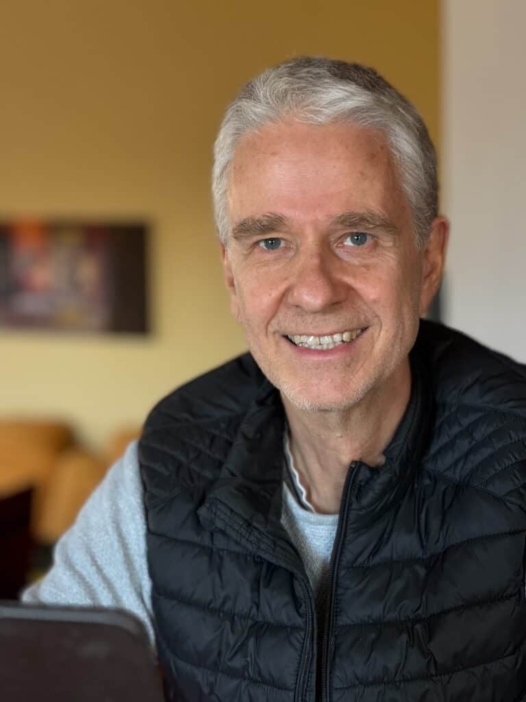 Saleem Matthias Riek sitzt am Laptop und schaut in die Kamera